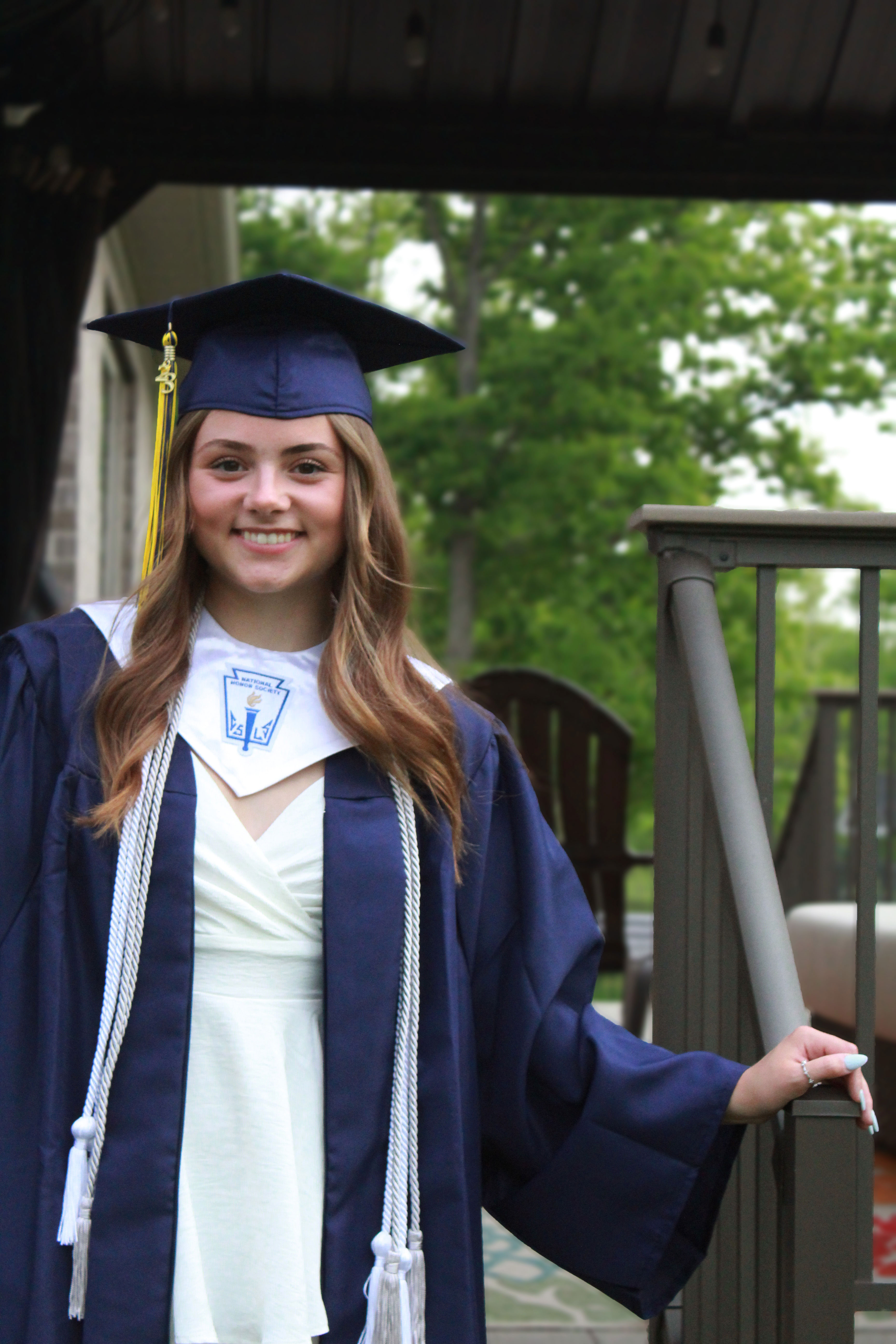 Image of a 2023 highschool gradutate on her back deck in a cap and gown